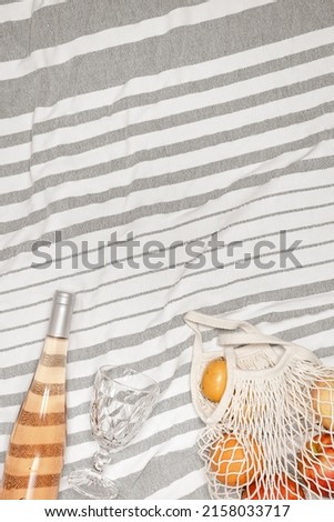 Summer holiday party, vacation, rest concept. Summer flat lay on stripes beach towel as background. Top view beach food and alcohol drink, bottle rose wine, wine glass, fresh fruits in mesh bag