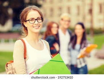 Summer Holidays, Education, Campus And Teenage Concept - Smiling Female Student In Black Eyeglasses With Folders And Group In The Back