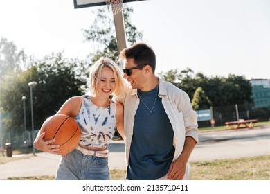 summer holidays, love and people concept - happy young couple with ball on basketball playground