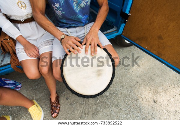 summer holidays, music, travel and people concept -\
close up of hippie friends having fun and playing tom-tom drum over\
minivan car