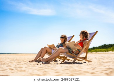 Summer holidays on beach with book. Two women of European beauty dressed in bikini and shorts reading books sitting on deckchairs on beach with white sand on beautiful sunny day. Relaxing on beach. - Powered by Shutterstock