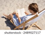 Summer holidays on beach. Woman of European beauty in white shirt reading book sitting on deckchair on background of white sand. Relaxing on beach. Closeup