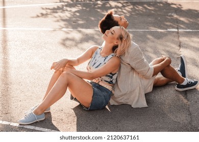 Summer Holidays And People Concept - Happy Young Couple Sitting Back To Back On Basketball Playground