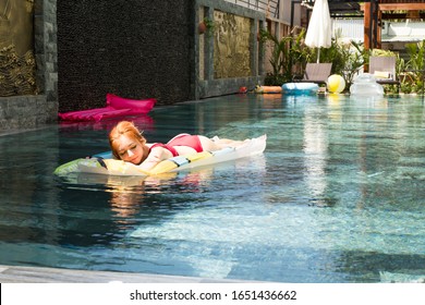 Summer Holidays Of Red Haired Beautiful Girl In Red Bikini Sunbathing In The Swimming Pool. Women Relaxing In The Pool After Busy Work On Sunny Weather.