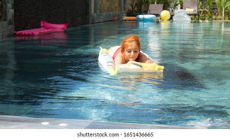 Summer Holidays Of Red Haired Beautiful Girl In Red Bikini Sunbathing In The Swimming Pool. Women Relaxing In The Pool After Busy Work On Sunny Weather.