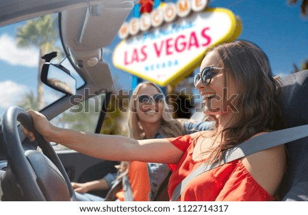 summer holidays, road trip and travel concept - happy young women driving in convertible car and laughing over welcome to fabulous las vegas sign background