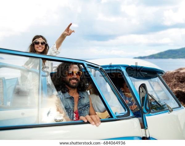 summer holidays, road trip, travel and people
concept - smiling young hippie friends in minivan car over island
and sea background