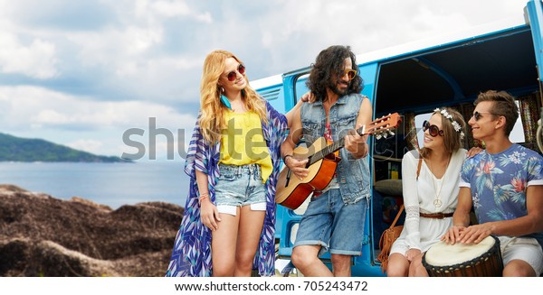 summer holidays, road trip, travel and\
people concept - happy young hippie friends with guitar and drum\
playing music at minivan car over island\
background