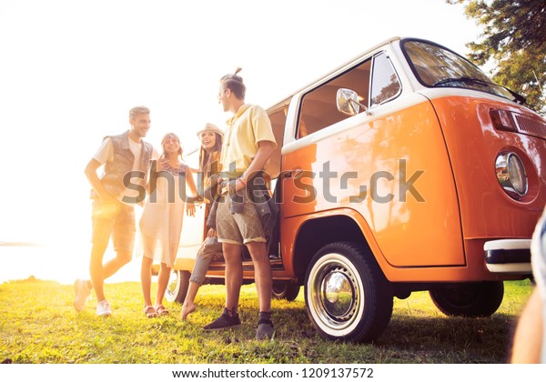 Summer\
holidays, road trip, vacation, travel and people concept - smiling\
young hippie friends having fun over minivan\
car