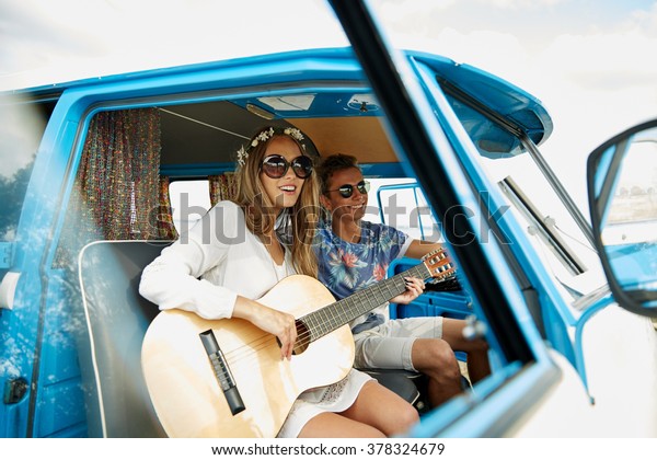 summer holidays, road trip, vacation, travel and\
people concept - smiling young hippie couple with guitar playing\
music in minivan car