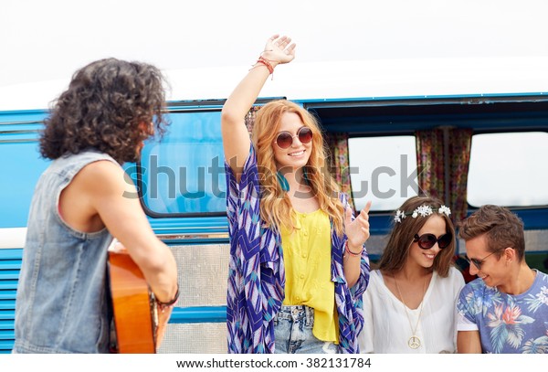summer holidays, road trip, vacation, travel and\
people concept - happy young hippie friends having fun and dancing\
over minivan car