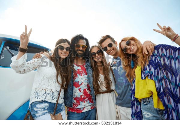 summer holidays, road trip, vacation, travel and\
people concept - smiling young hippie friends over minivan car\
showing peace hand sign