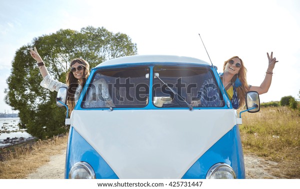 summer holidays, road trip, vacation, travel and
people concept - smiling young hippie women driving minivan car and
showing peace gesture