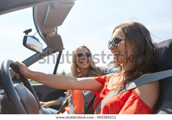 summer holidays, road trip, vacation, travel and\
people concept - happy young women driving in in cabriolet car and\
laughing