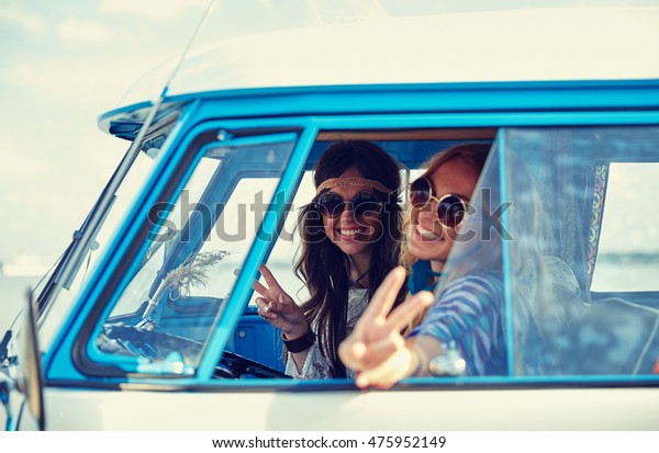 summer holidays, road trip, vacation, travel and\
people concept - smiling young hippie women driving minivan car and\
showing peace gesture