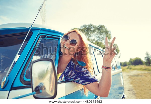 summer holidays, road trip, vacation, travel and\
people concept - smiling young hippie woman driving minivan car and\
showing peace gesture