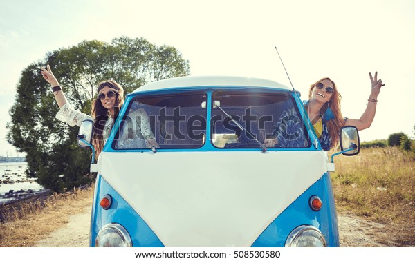 summer holidays, road trip, vacation, travel and\
people concept - smiling young hippie women driving minivan car and\
showing peace gesture