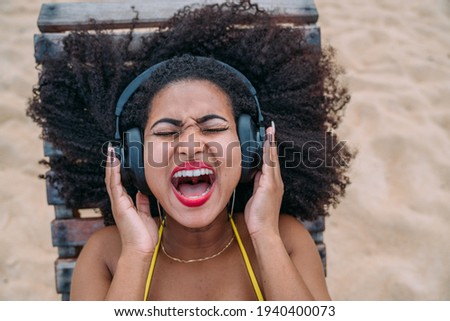 summer holidays, technology and internet concept. latin american woman listening music with headphone and sunning on the beach