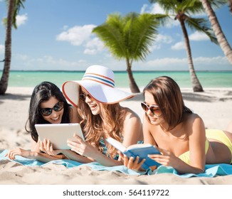 summer holidays, technology, people, travel and internet concept - happy young women in bikinis with tablet pc and book sunbathing over exotic tropical beach with palm trees and sea shore background