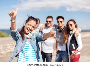 Summer Holidays And Teenage Concept - Teenage Girl In Sunglasses And Headphones Hanging Out With Friends Outside And Showing Thumbs Up