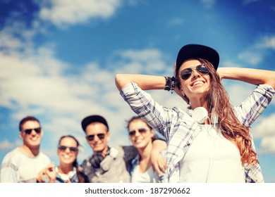 Summer Holidays And Teenage Concept - Teenage Girl In Sunglasses, Cap And Headphones Hanging Out With Friends Outside