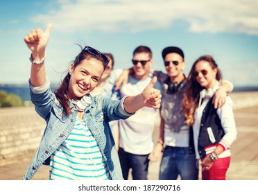 summer holidays and teenage concept - teenage girl in sunglasses and headphones hanging out with friends outside and showing thumbs up