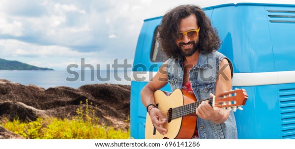 summer holidays, travel, music and people\
concept - young hippie man playing guitar at minivan car over\
island and sea\
background