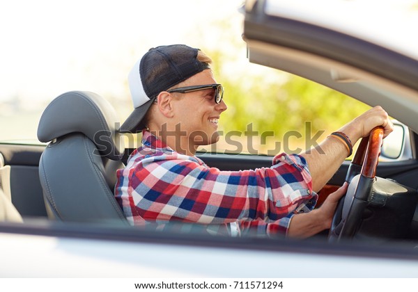 summer holidays, travel, road trip and people concept\
- happy smiling young man in sunglasses and cap driving convertible\
car