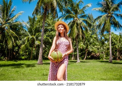 Summer holidays, vacation concept. Smiling travel women holding young green coconut among exotic tropical palm trees. Beautiful girl under branches of the palm trees, relaxing on travel vacation.