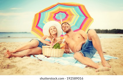 summer, holidays, vacation and happy people concept - smiling couple lying on the beach under colorful umbrella and sunbathing