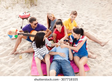 Summer Holidays, Vacation, Music, Happy People Concept - Group Of Happy Friends Having Picnic And Playing Guitar On Beach, Drinking Non-alcoholic Beer Or Soda Lemonade