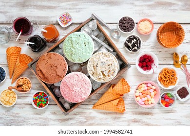 Summer Ice Cream Bar With A Selection Of Ice Cream Flavors And Dessert Toppings. Top View Table Scene On A Rustic White Wood Background.