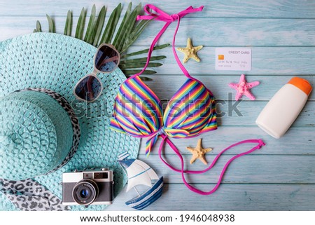 Summer items fashion tourism woman swimsuit Bikini with sunblock and big hat. Traveler tour pay credit card for travel and vacations trip in the holiday on blue wood background, top view. 