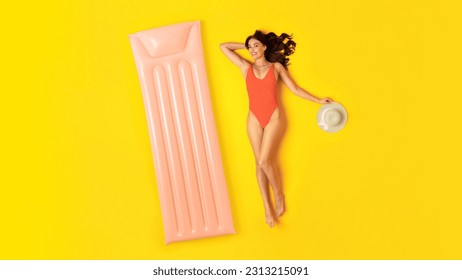 Summer Joy. Cheerful Young Lady In Orange Swimwear Lying Near Inflatable Lilo, Sunbathing And Relaxing Having Pool Party On Yellow Studio Background, Smiling To Camera. View From Above, Panorama