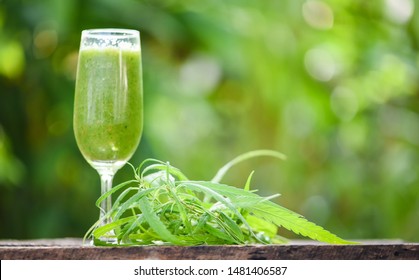 summer juice with green fruit smoothies in glass with cannabis leaf marijuana plant on wooden table green background / cannabis food , selective focus