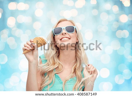summer, junk food and people concept - young woman or teenage girl in sunglasses eating ice cream over blue holidays lights background