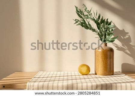 Summer kitchen home interior decor, ceramic vase, lemon on wooden table with stripped linen tablecloth, empty beige wall background with natural sunlight shadows, cottage retro aesthetic.