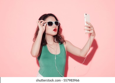 Summer Lady. Beautiful Asian Girl With Professional Makeup And Stylish Hairstyle Singing And Dancing While Listening To Music On Pink Background.