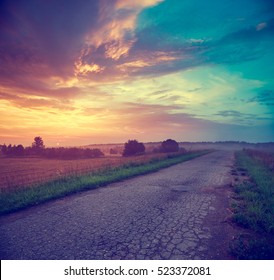 Summer Landscape with Field and Country Road Leading in the Fog. Dramatic Sky at Sunset Background. Beautiful Nature Background. Toned Photo with Copy Space.