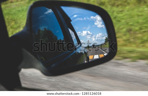 summer\
landscape in the reflection of the side mirror of the car. View of\
the road in the journey . blue sky and\
clouds