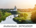 Summer landscape in Suzdal. Church of Elijah the Prophet on the bank of river Kamenka. Tourists on SUP boards float on the river. Russia, Vladimir region, Golden Ring of Russia. The bright setting sun