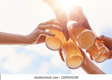 Summer, leisure, celebration and drinking concept. Close up shot of four hands clink bottles with lemonade or energy drink over blue sky and sunshine, celebrate starting vacations, have picnic - Powered by Shutterstock