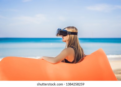 Summer lifestyle portrait of pretty girl sitting on the orange inflatable sofa and uses virtual reality headset on the beach of tropical island. Relaxing and enjoying life on air bed - Powered by Shutterstock