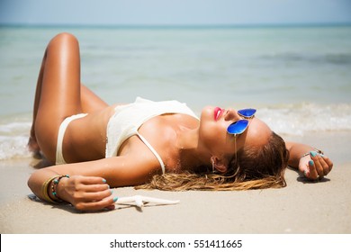 Summer lifestyle portrait of pretty young girl with tanned sexy body. Enjoying life, smiling and lying in the clear sea water on the beach of the tropical island . Wearing white bikini and sunglasses