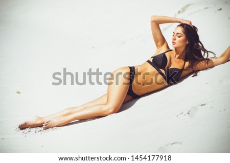 Summer lifestyle portrait of pretty young suntanned woman. Enjoying life, smiling and lying on the beach of the tropical island. Wearing stylish bikini