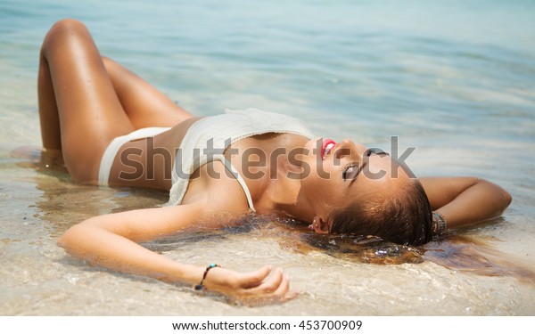色っぽい体を日焼けさせた美しい若い女の子の夏のライフスタイルのポートレート 熱帯の島の浜辺の清い海の水の中で 人生を楽しみ にこにこ笑み 横たわる 白いビキニを着る の写真素材 今すぐ編集