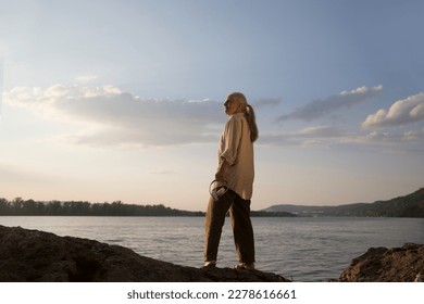 Summer lifestyle portrait senior woman  with gray hair with headphones relaxes on the seashore at sunset. spends time in nature in summer. Audio healing. meditation. banner. copy space. greyhairdontca - Powered by Shutterstock