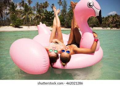 Summer lifestyle portrait of two pretty girls friends having fun on air mattress in the ocean. Wearing bikini and mirrored sunglasses. Smiling and doing yoga. Positive emotions, bright colors 