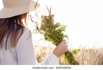 Summer lifestyle portrait of a woman holding a bouquet of field flowers, herbs. She is standing on a field of grass.Happiness and love concept. Copy space