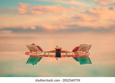 Summer love and romance table set-up for a romantic dinner meal with infinity pool reflection chairs under sunset sky and sea in the background. Luxury destination dining, romantic dinner for couples